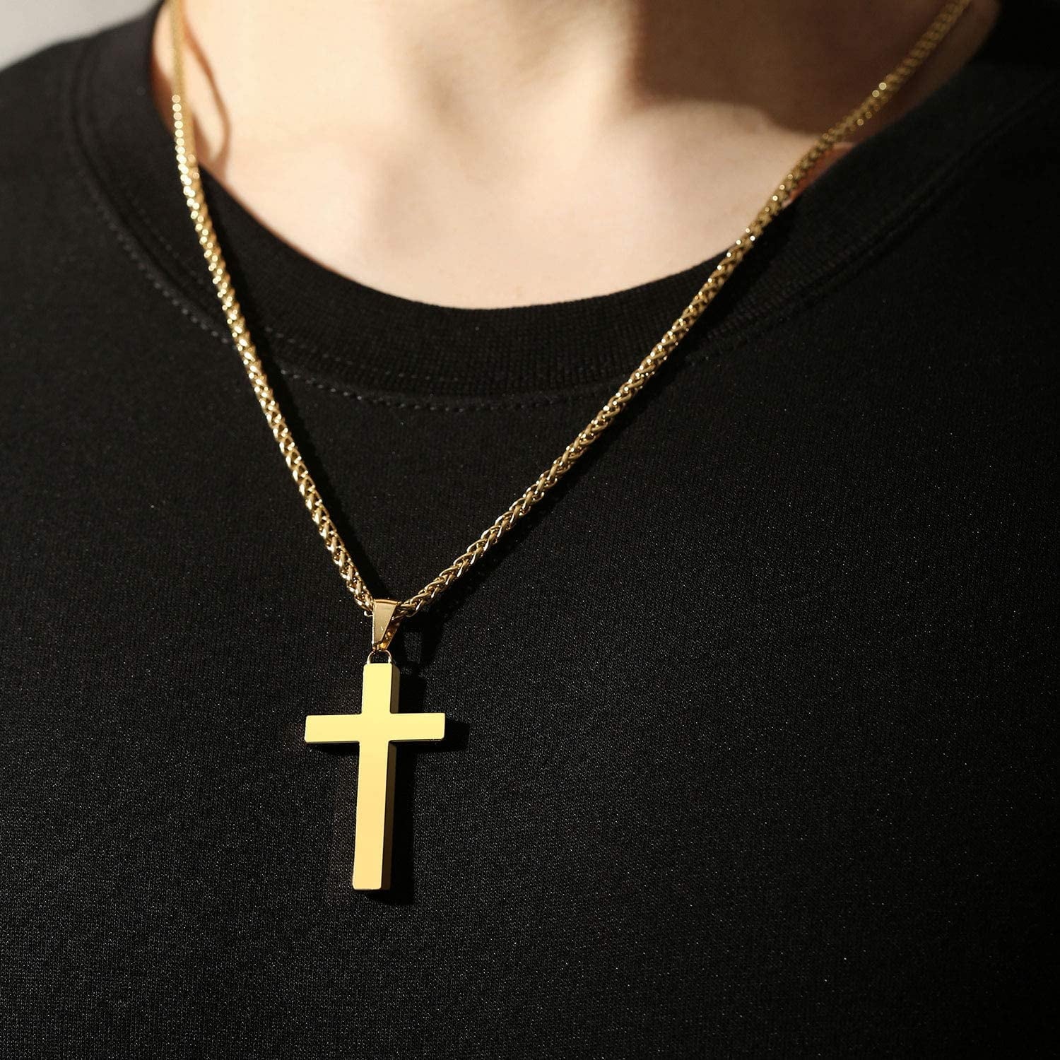 Gold cross pendant necklace with chain, worn around the neck over a black shirt.