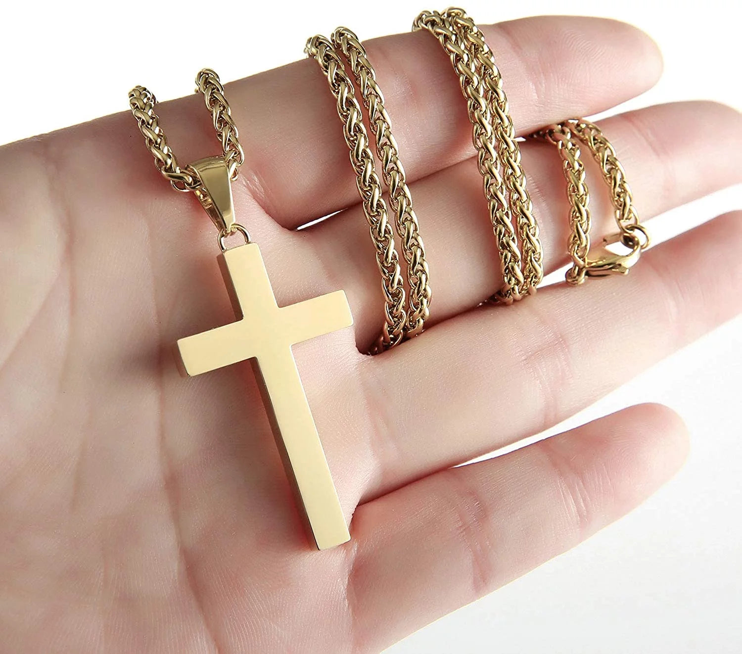 Gold-toned cross pendant necklace on a thick chain held in a hand.
