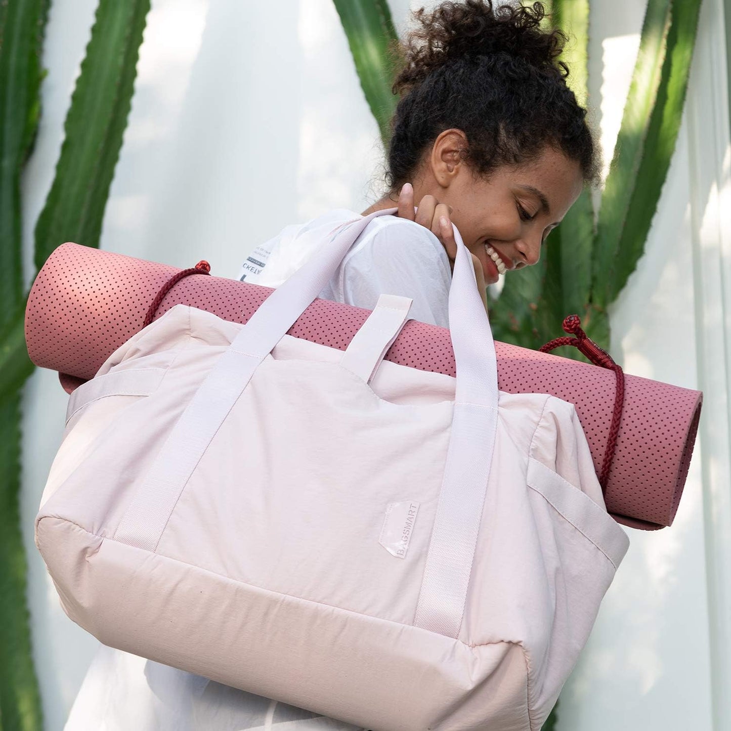 Pink women's gym bag with a rolled yoga mat on top, carried by a smiling woman.