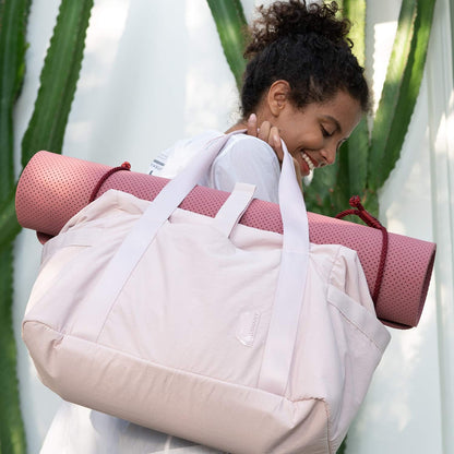Pink women's gym bag with a rolled yoga mat on top, carried by a smiling woman.